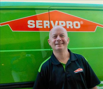 Smiling male employee standing next to a SERVPRO vehicle wearing a black SERVPRO shirt.