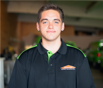 Smiling male employee wearing a green SERVPRO shirt standing in front of a SERVPRO vehicle.