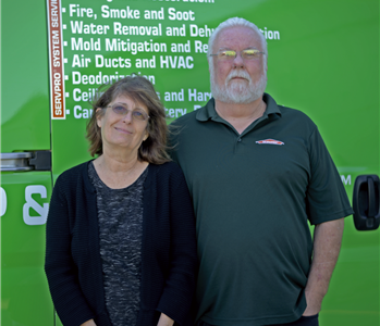 Husband and wife team standing in front of a SERVPRO vehicle.
