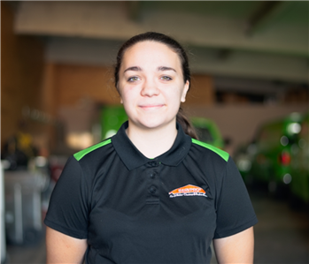 Smiling female employee wearing a green SERVPRO shirt standing in front of a SERVPRO vehicle.